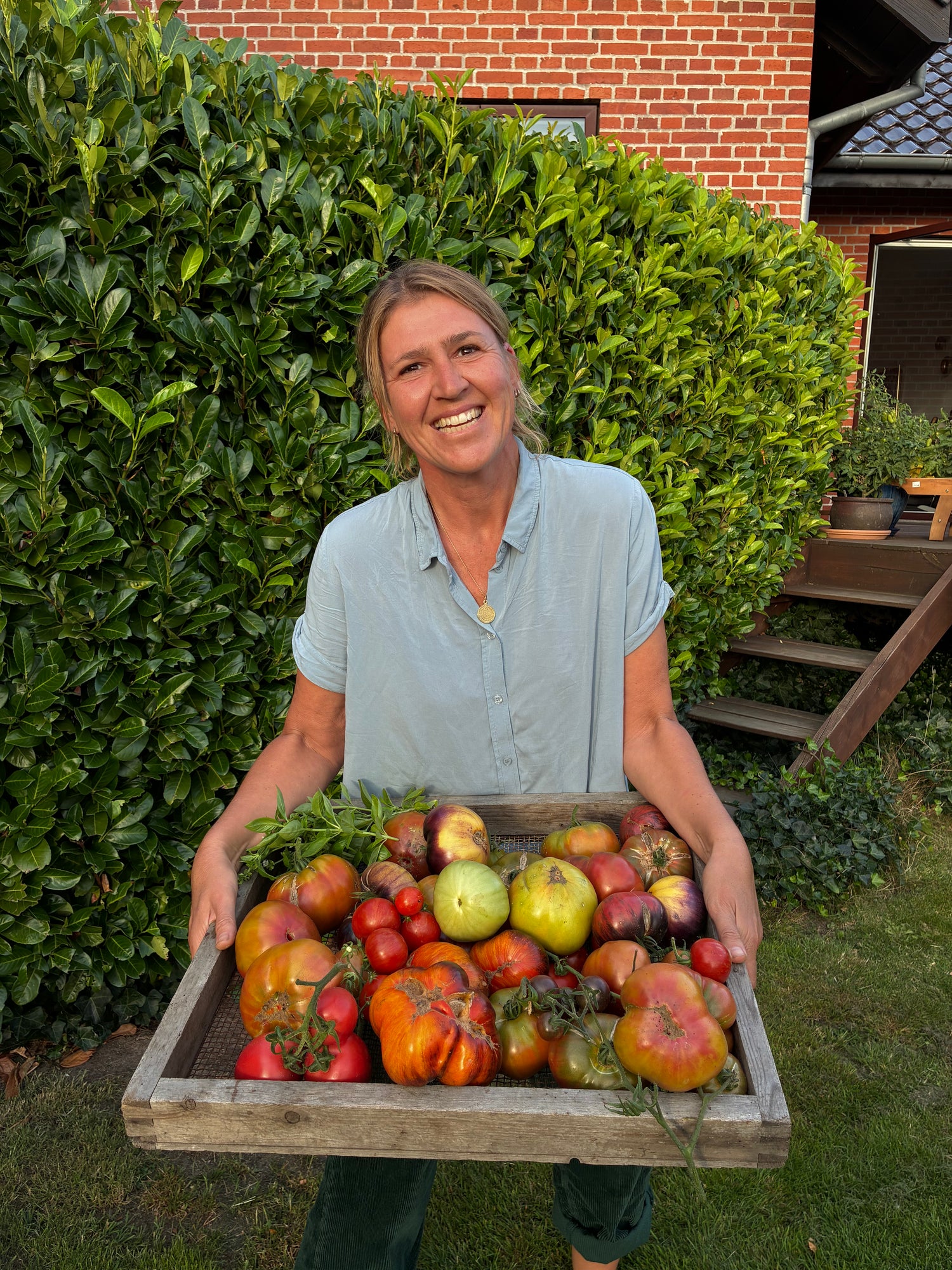 Smilende kvinde holder træbakke med tomater i hænderne.
